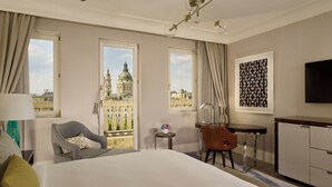Habitación de hotel con cama, escritorio, silla, televisión y vista a un edificio histórico.