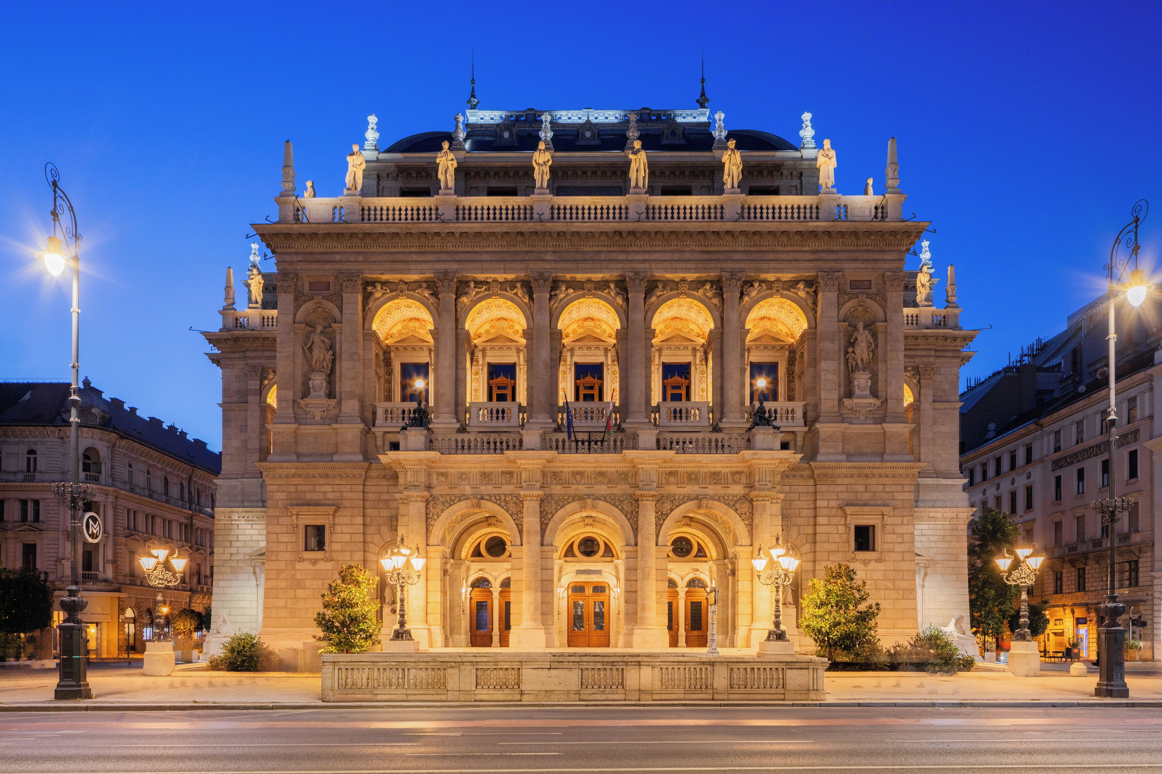 Un edificio histórico con arquitectura ornamentada, que incluye un balcón con estatuas y una entrada central con columnas.