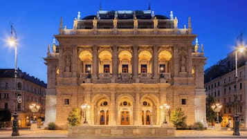 Un edificio histórico con arquitectura ornamentada, que incluye un balcón con estatuas y una entrada central con columnas.
