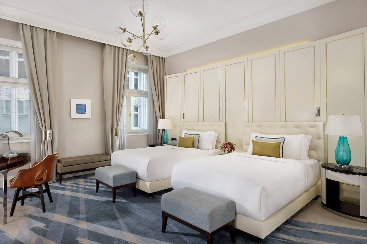 A hotel room with two beds, a bench, a desk, and a chair.