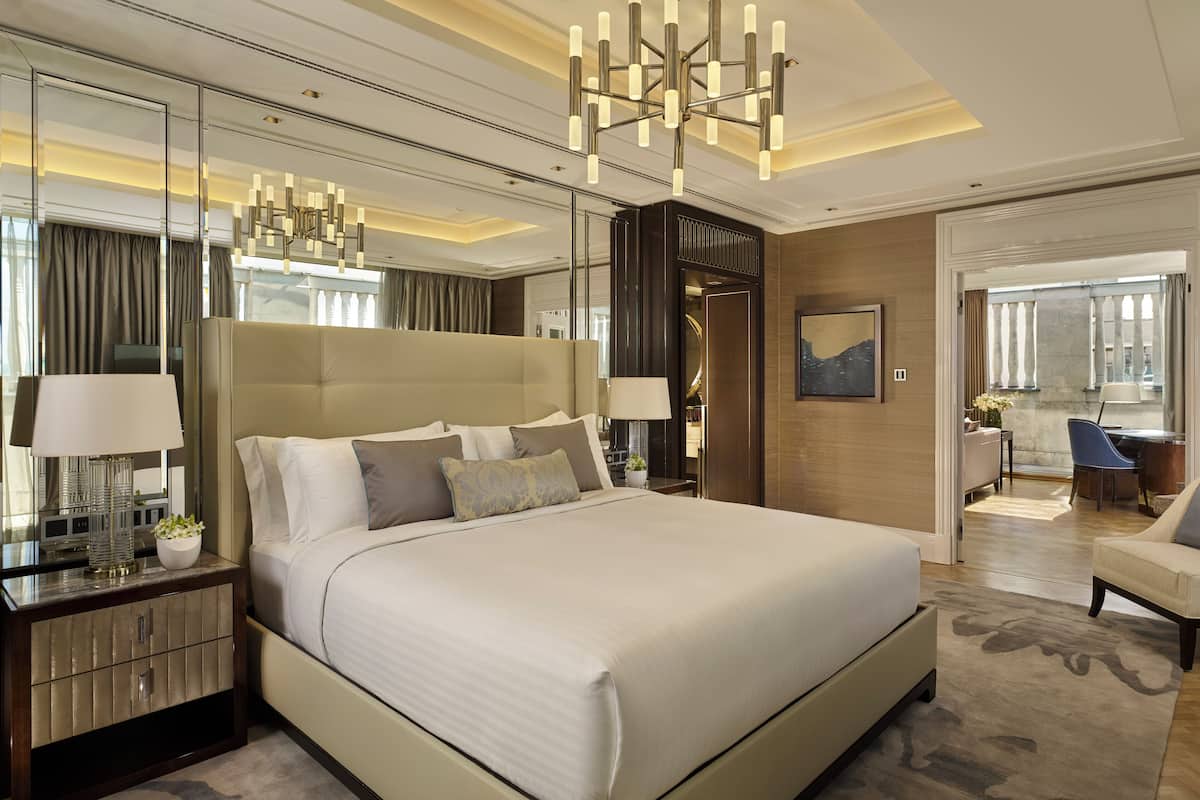 A modern hotel room with a large bed, a sitting area with a chair, and a desk.