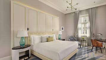 A hotel room with a large bed, bedside tables, a desk, a chair, and a chandelier.