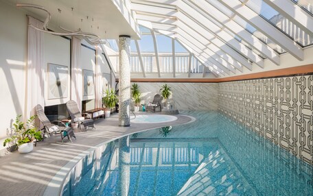 A large indoor swimming pool with a glass ceiling, lounge chairs, and potted plants.