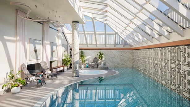Una amplia piscina interior con techo de cristal, sillones de descanso y plantas en macetas.
