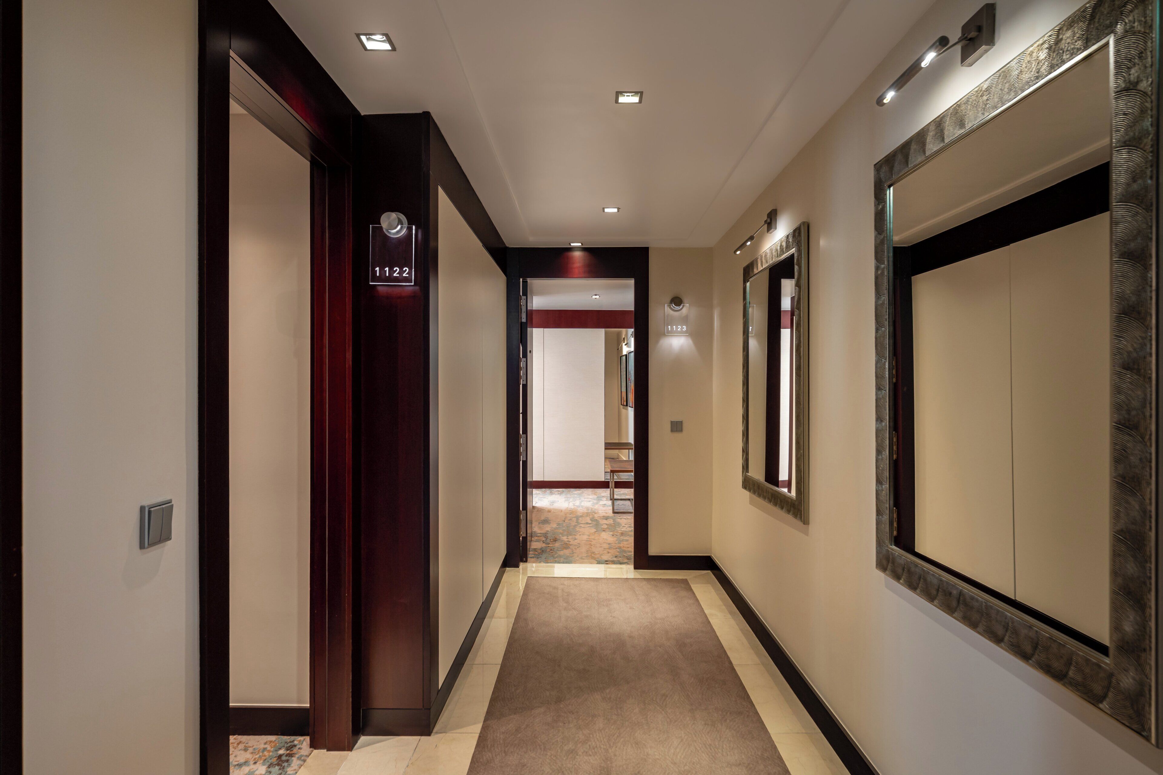 A hotel hallway with a carpeted floor, wooden doors, and a number sign indicating room 1122.