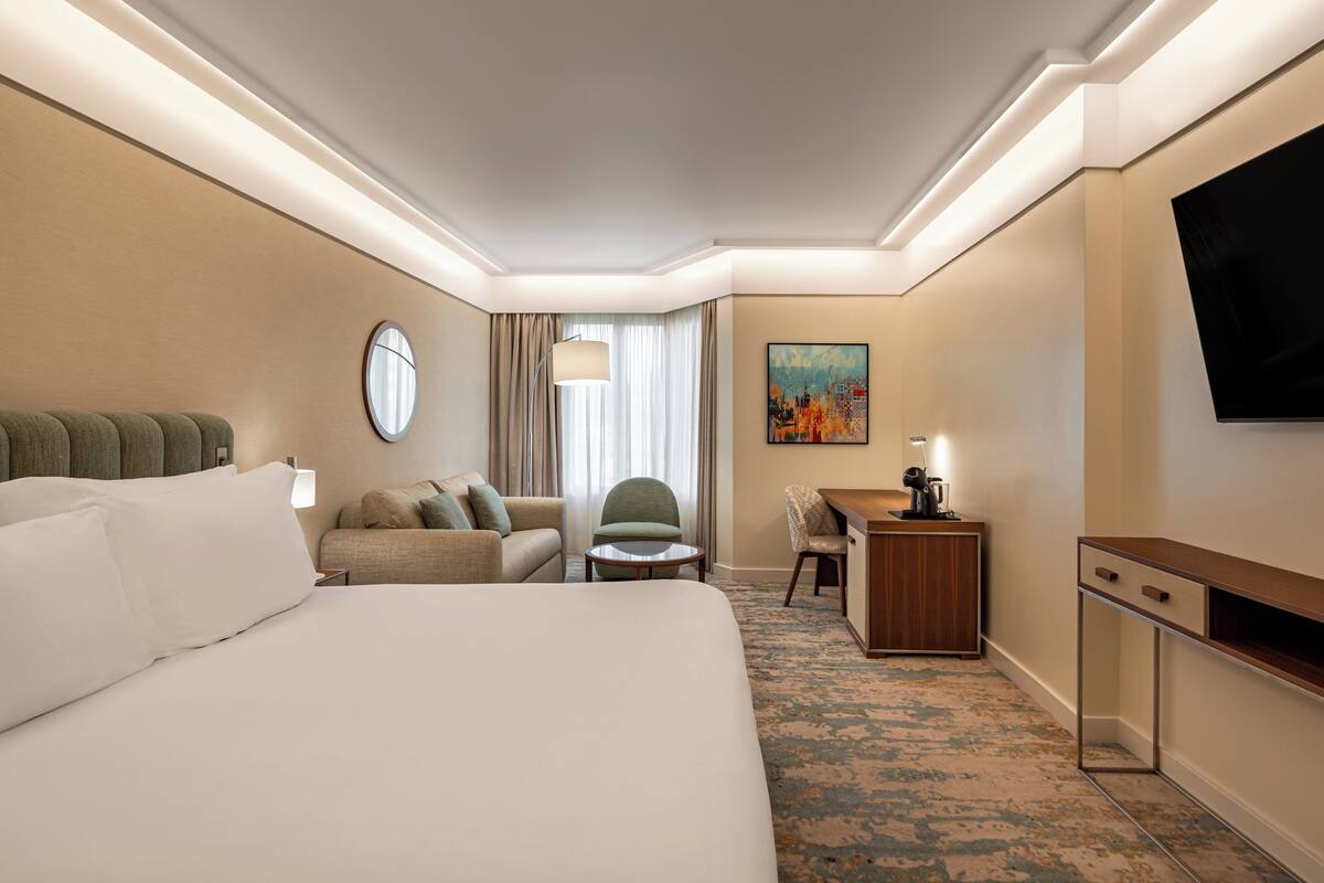 A hotel room with a large bed, a desk, a chair, a television, and a painting on the wall.