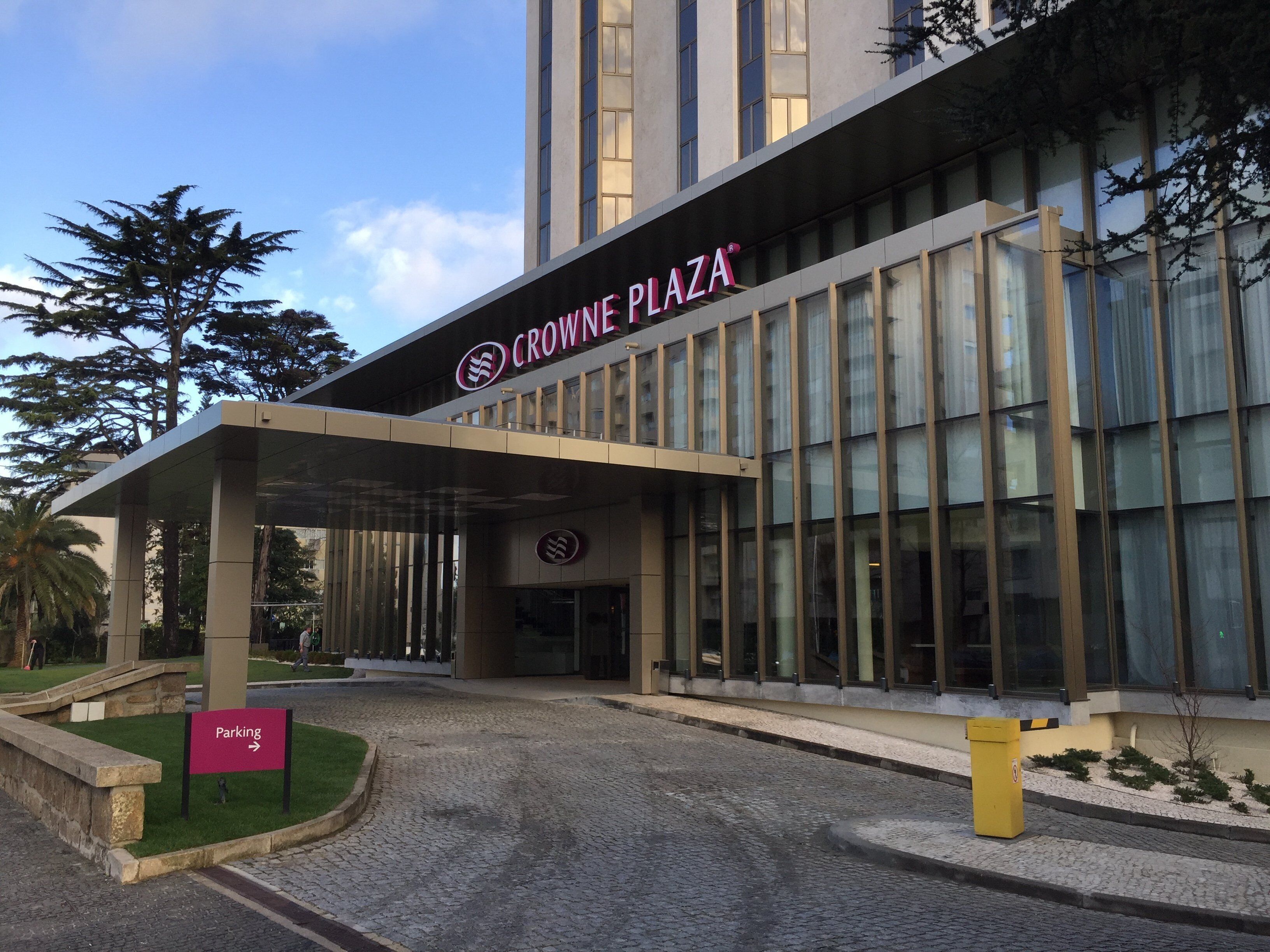 A modern building with a sign reading 'CROWNE PLAZA' and a 'Parking' sign indicating the direction.
