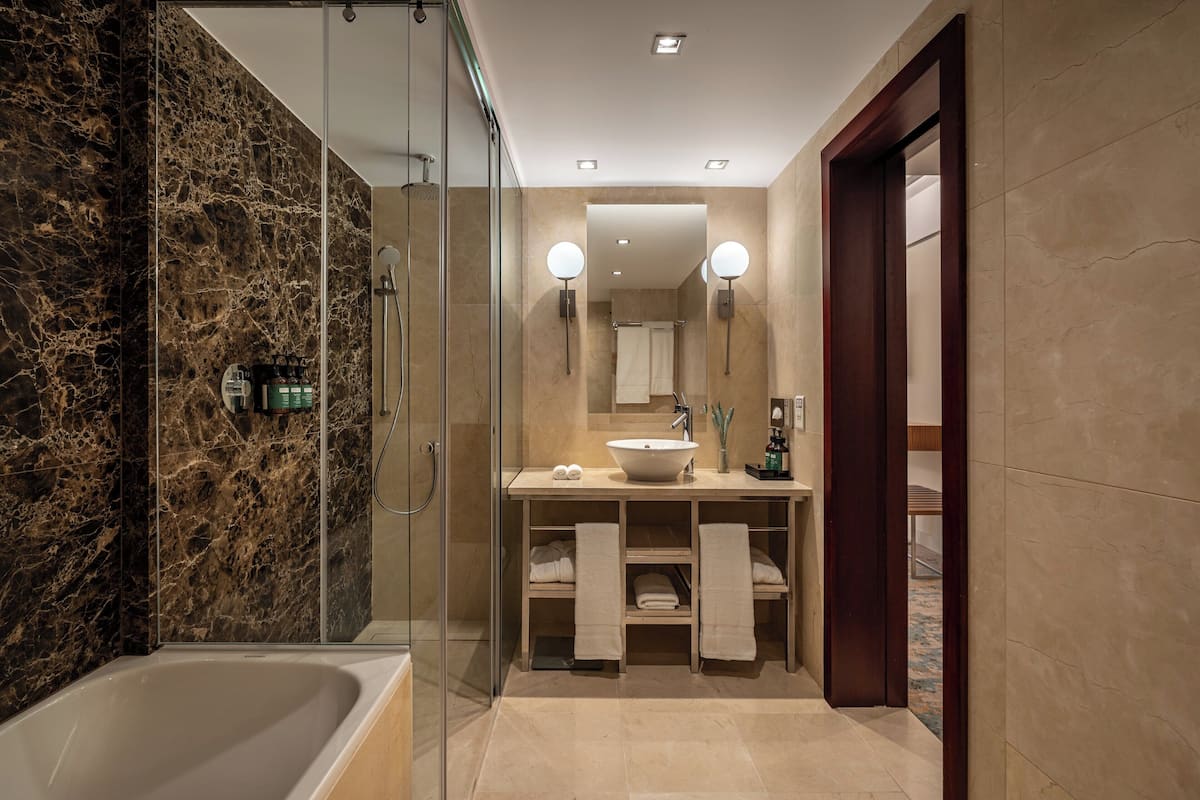 A modern bathroom with a glass-enclosed shower, a bathtub, a vanity with a sink, and two wall-mounted lights.