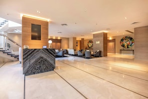 A modern hotel lobby with a marble reception desk, seating area, and a staircase. - Crowne Plaza Porto by IHG (Porto)