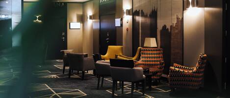 A hotel lobby with a reception desk, seating area with chairs, and a wall-mounted television.