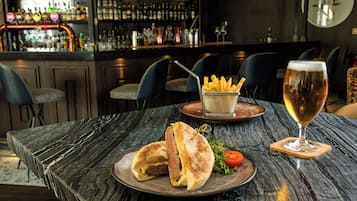 A dining table with a sandwich, fries, a glass of wine, and a bar in the background.