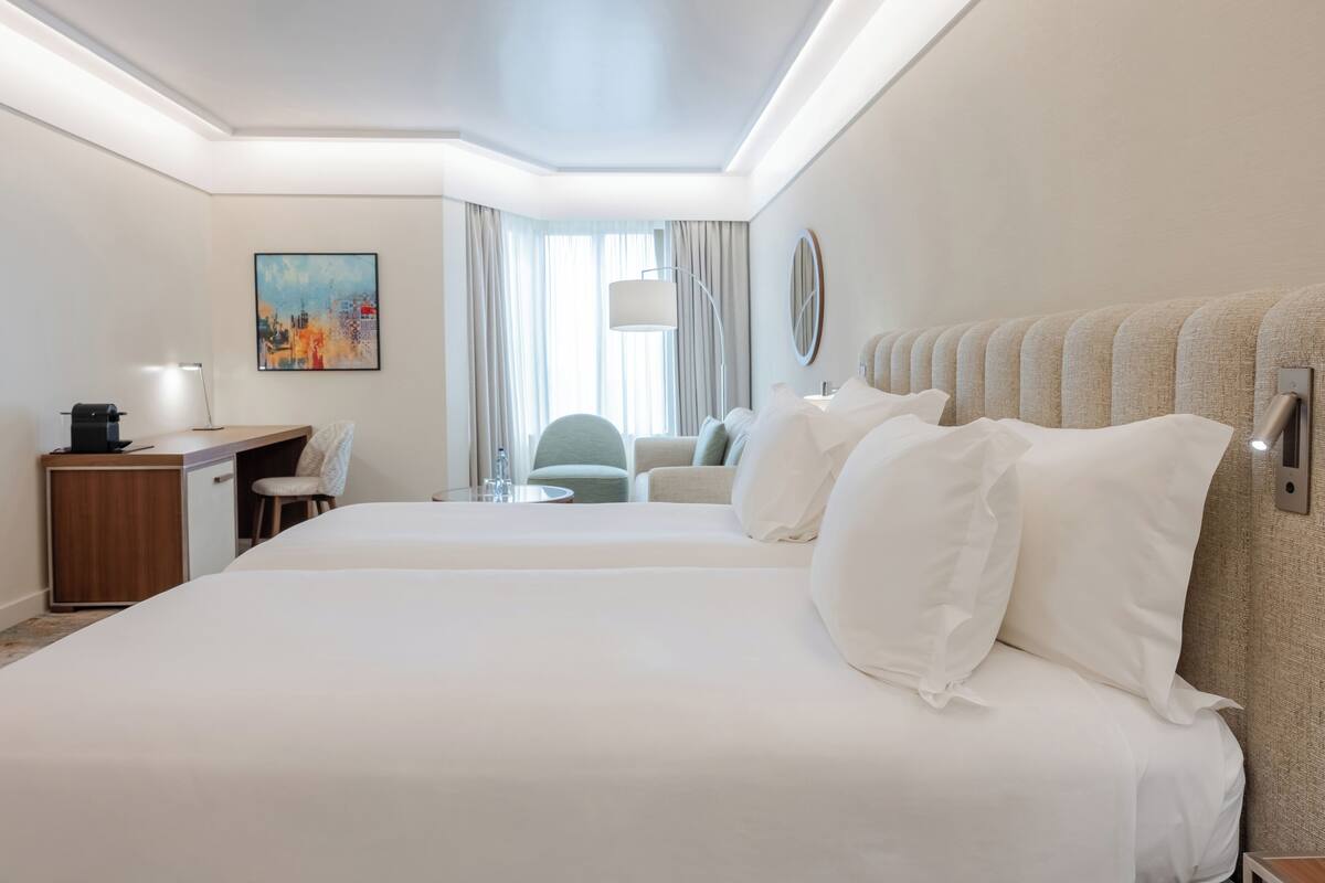 A hotel room with a large bed, a desk, a chair, a lamp, and a painting on the wall.