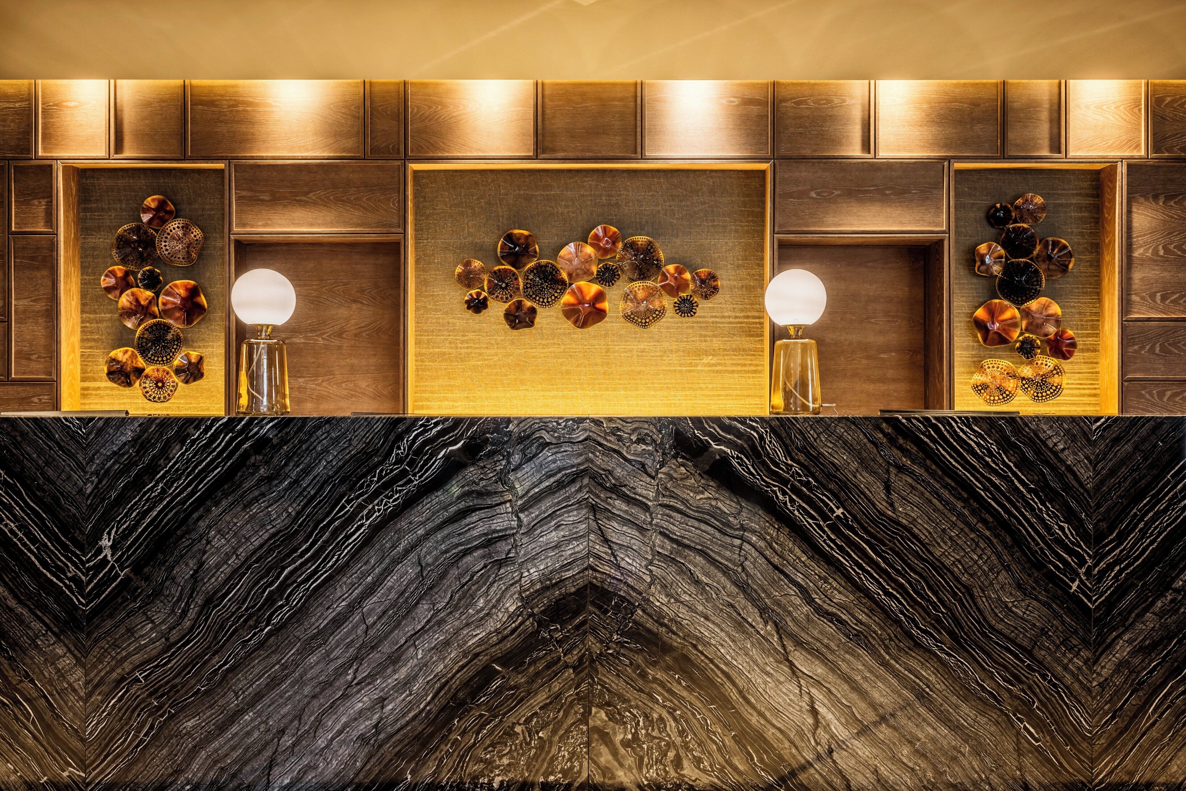 Un baño moderno con encimera de mármol negro, paneles de madera y detalles decorativos de vidrio.