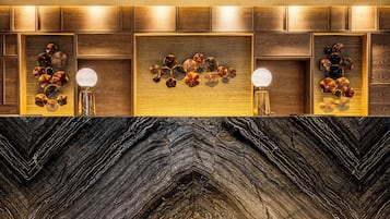 Un baño moderno con encimera de mármol negro, paneles de madera y detalles decorativos de vidrio.