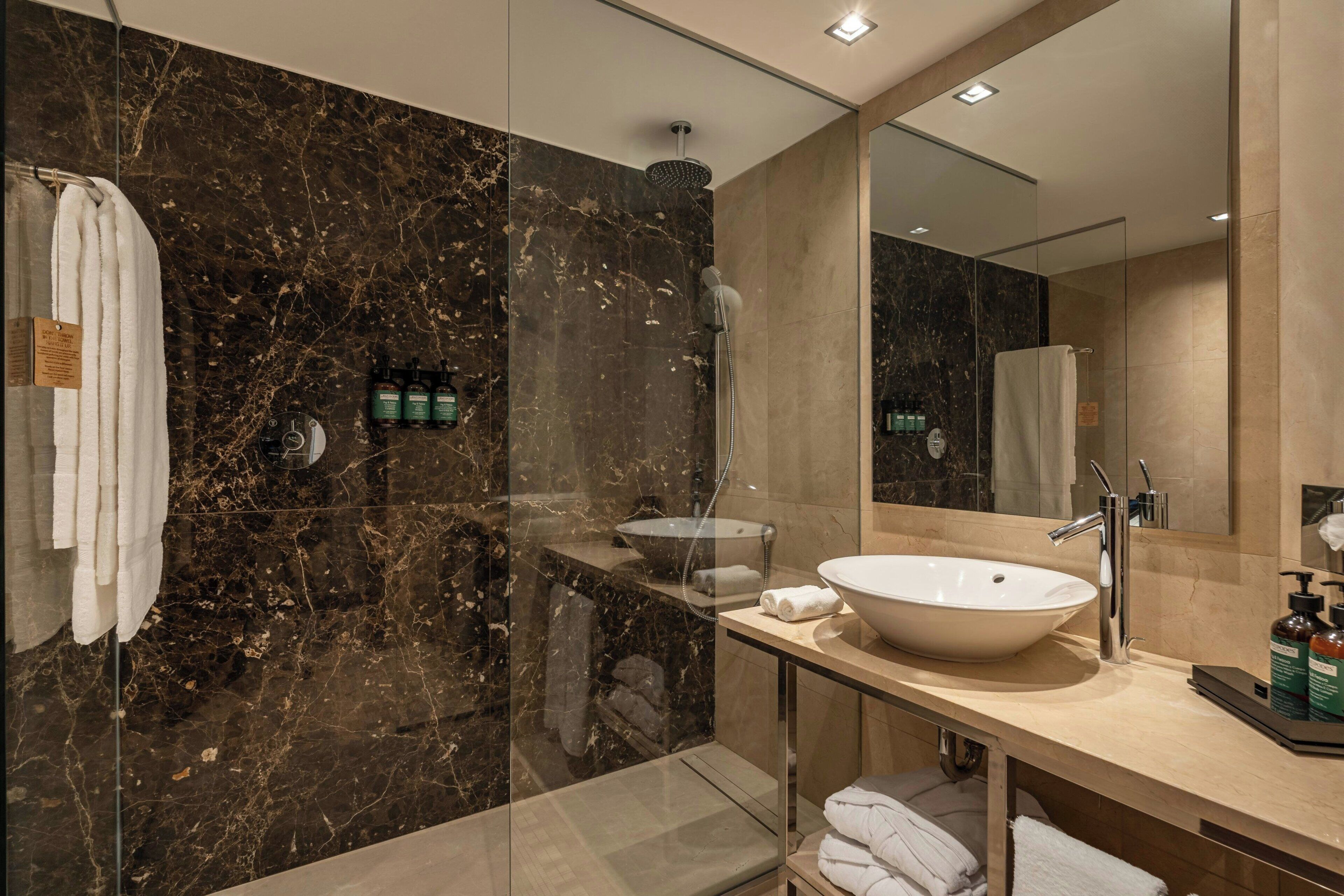 A modern bathroom with a glass-enclosed shower, a large sink, and a vanity with toiletries.