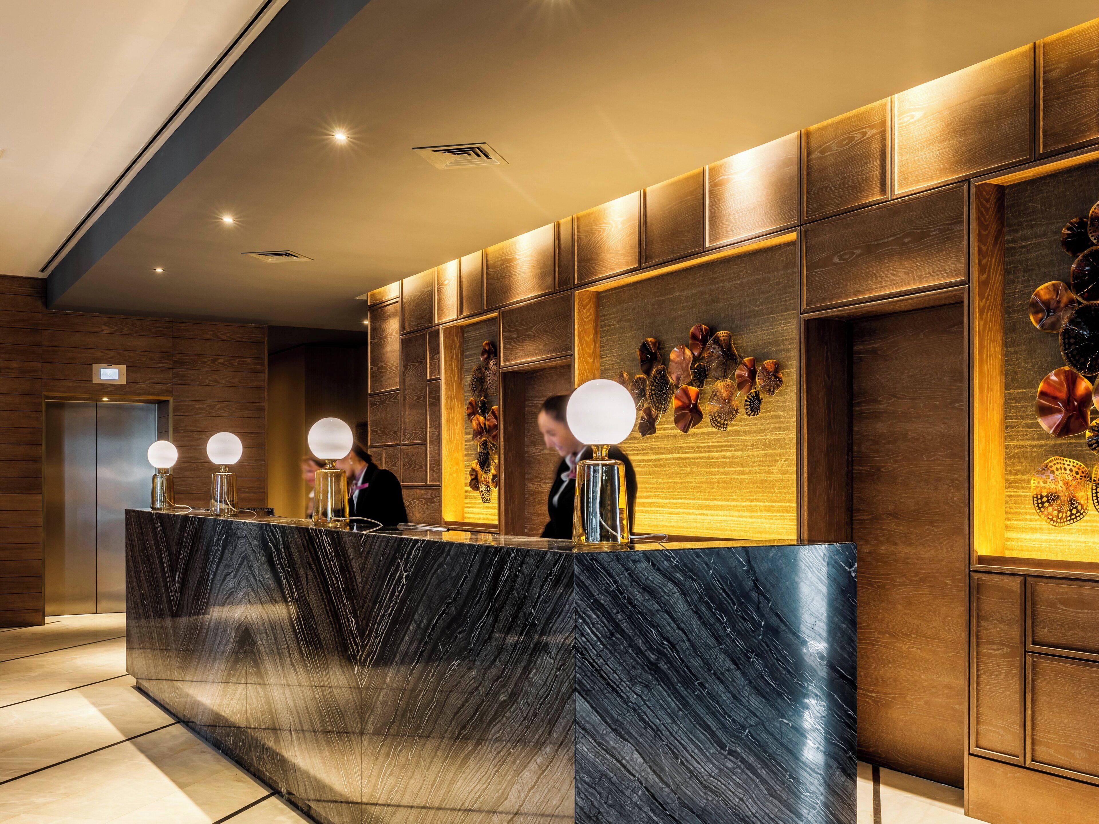 A reception desk with a marble top, wooden paneling on the walls, and a decorative wall piece.