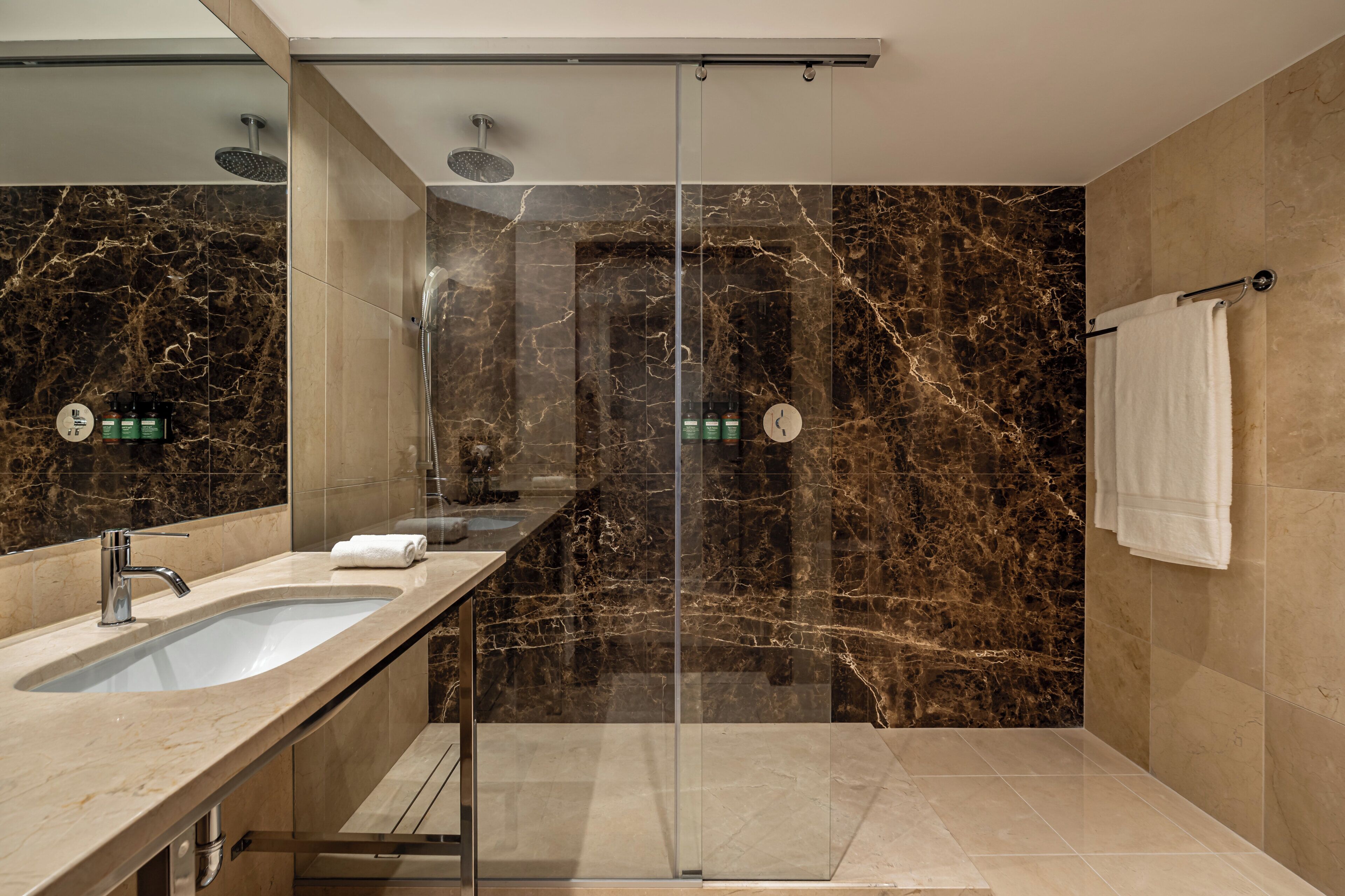 A modern bathroom with a glass-enclosed shower, a marble-tiled wall, a sink with a mirror, and a towel rack.