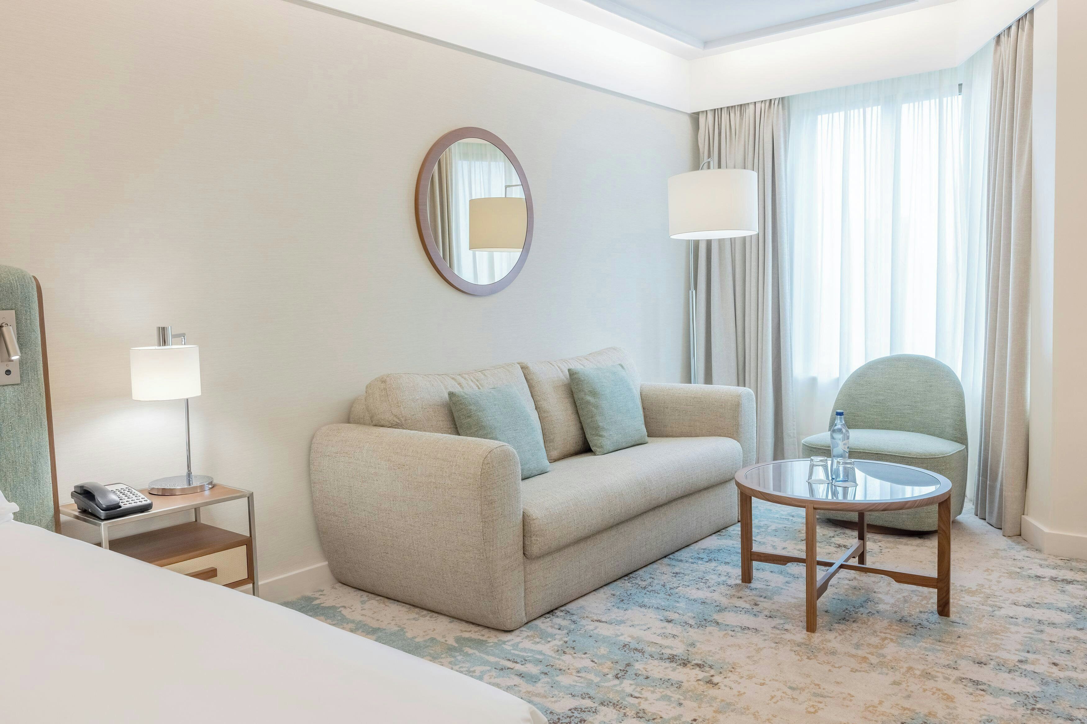 Una habitación de hotel con un sofá, una mesita, una lámpara, un espejo y una silla.