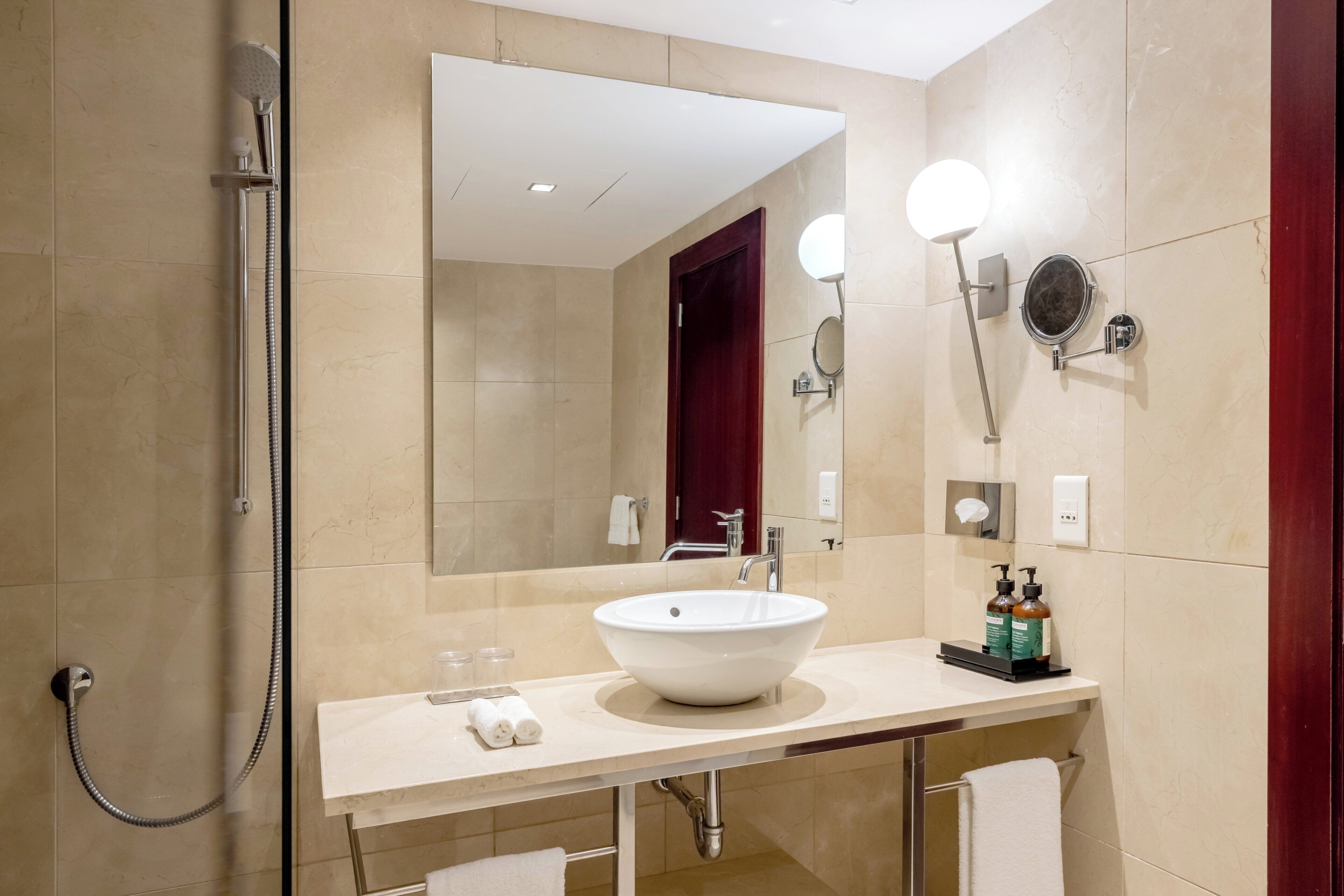 A modern bathroom with a large mirror, a white sink, and a handheld showerhead.