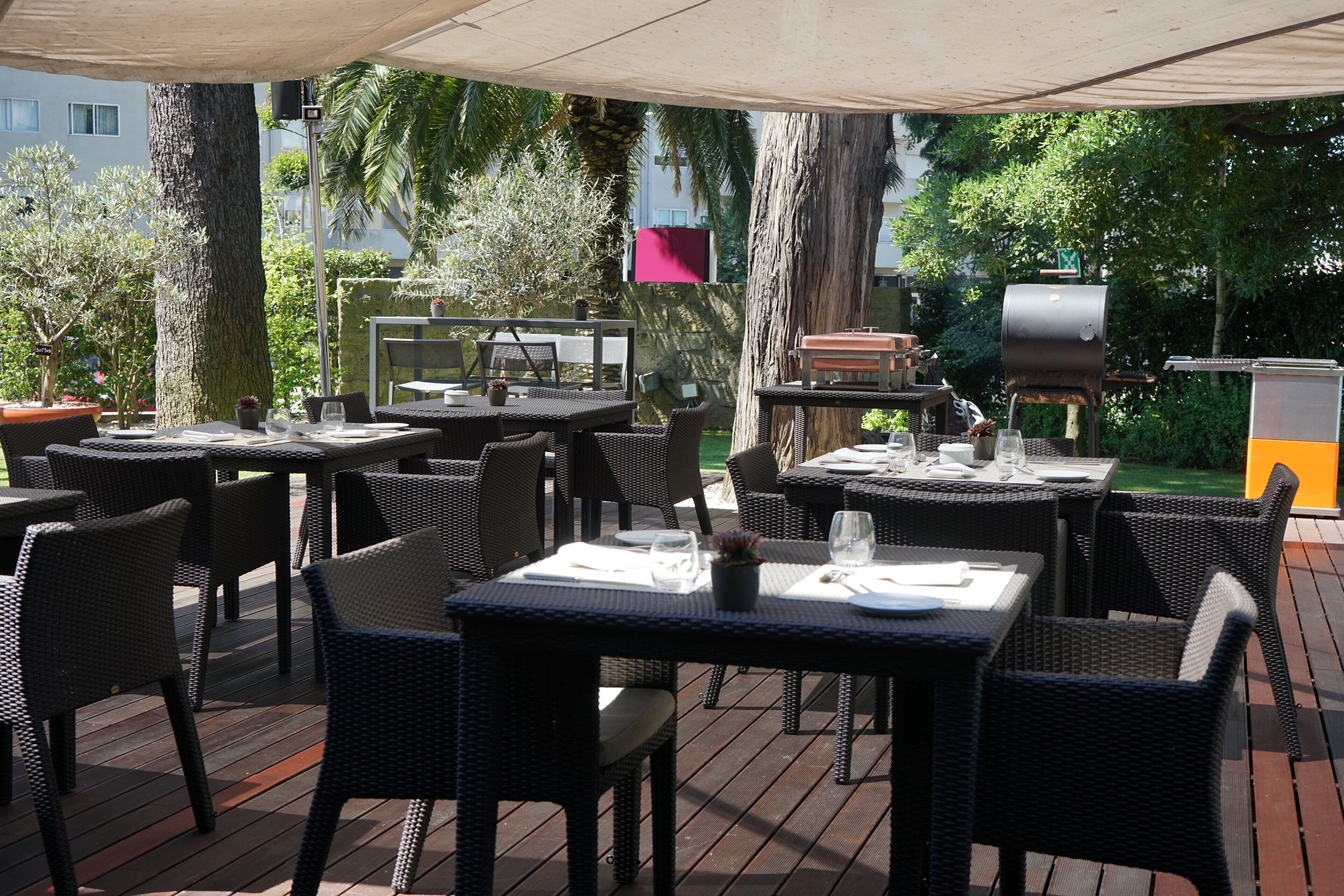 An outdoor patio with tables and chairs, a barbecue grill, and a large umbrella providing shade.
