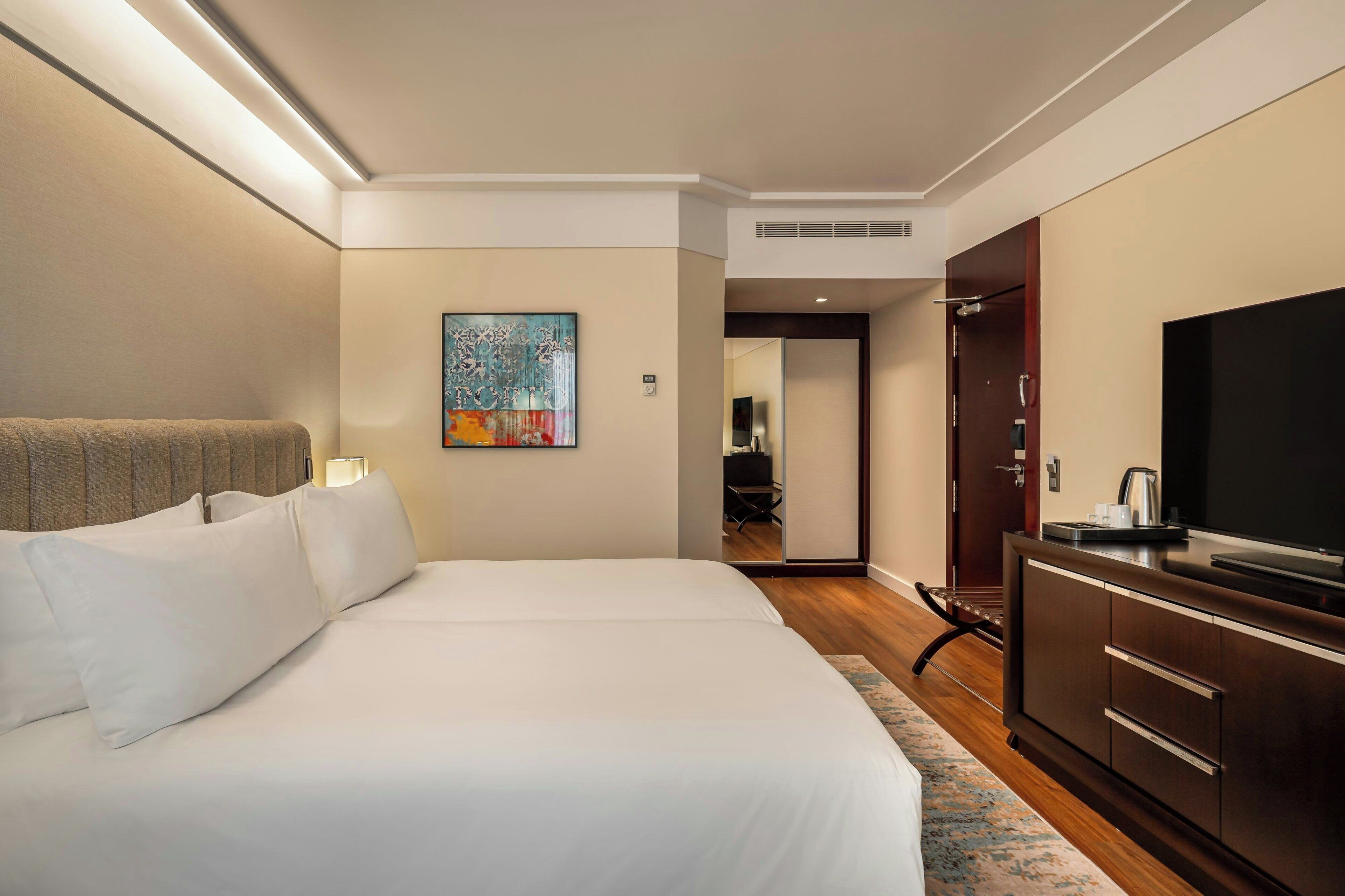 A hotel room with a large bed, a flat-screen TV, a painting on the wall, and a wooden cabinet.