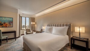 Habitación de hotel con una cama grande, dos mesitas de noche, un escritorio, una silla y una ventana con cortinas.