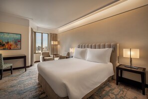 Habitación de hotel con una cama grande, dos mesitas de noche, un escritorio, una silla y una ventana con cortinas.