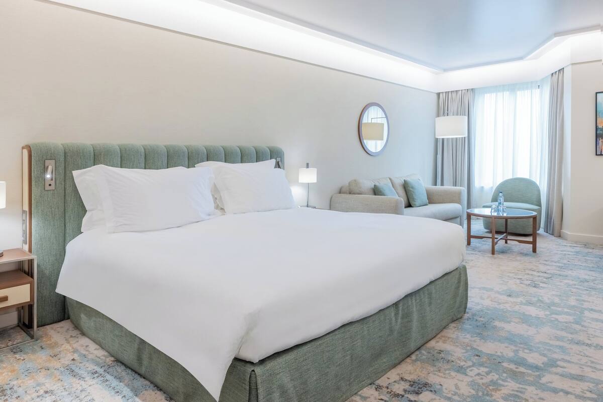 A hotel room with a large bed, a sofa, a round table, and a lamp.