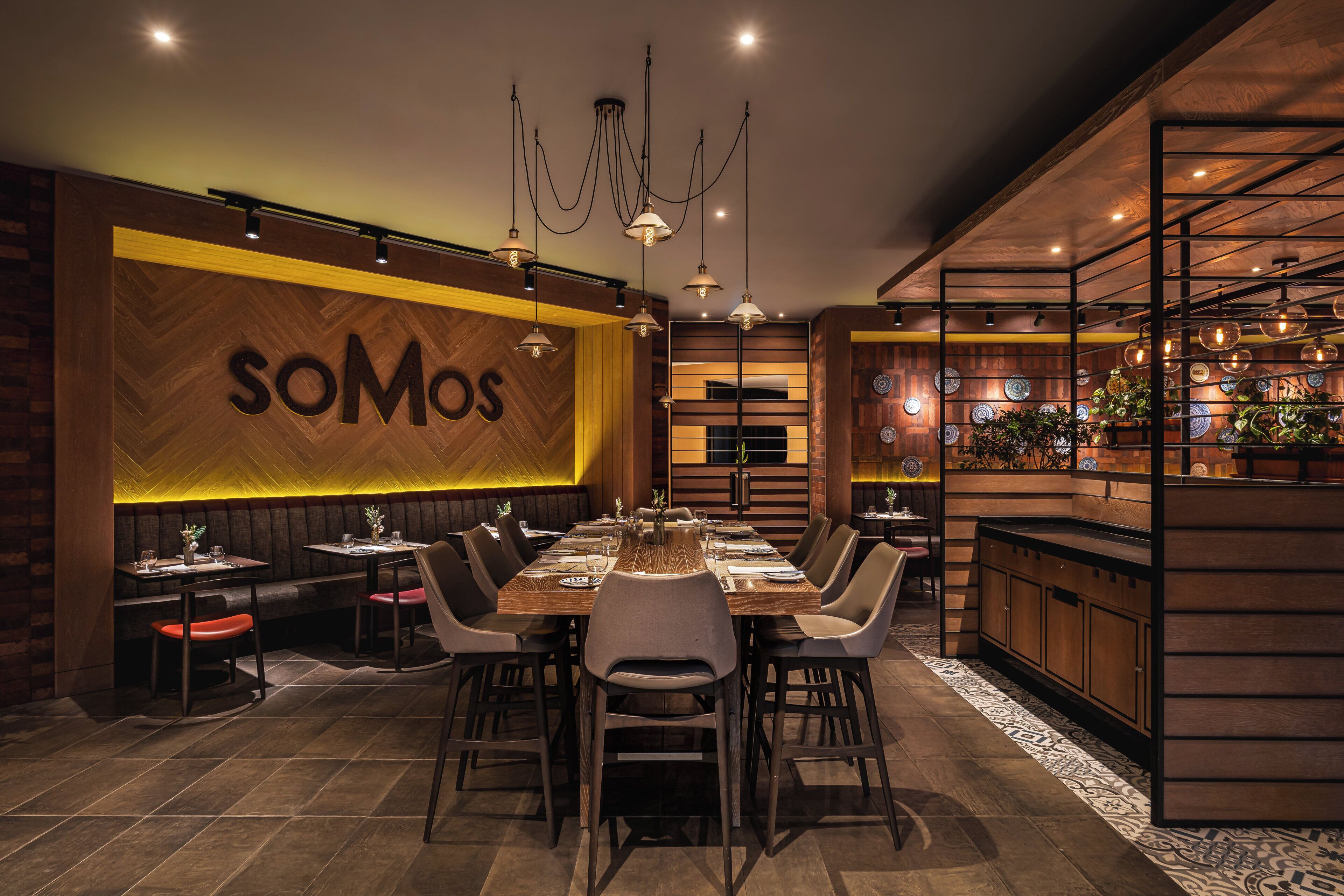 A restaurant interior with a large wooden wall, a dining table set for six, and a bar area with plants.