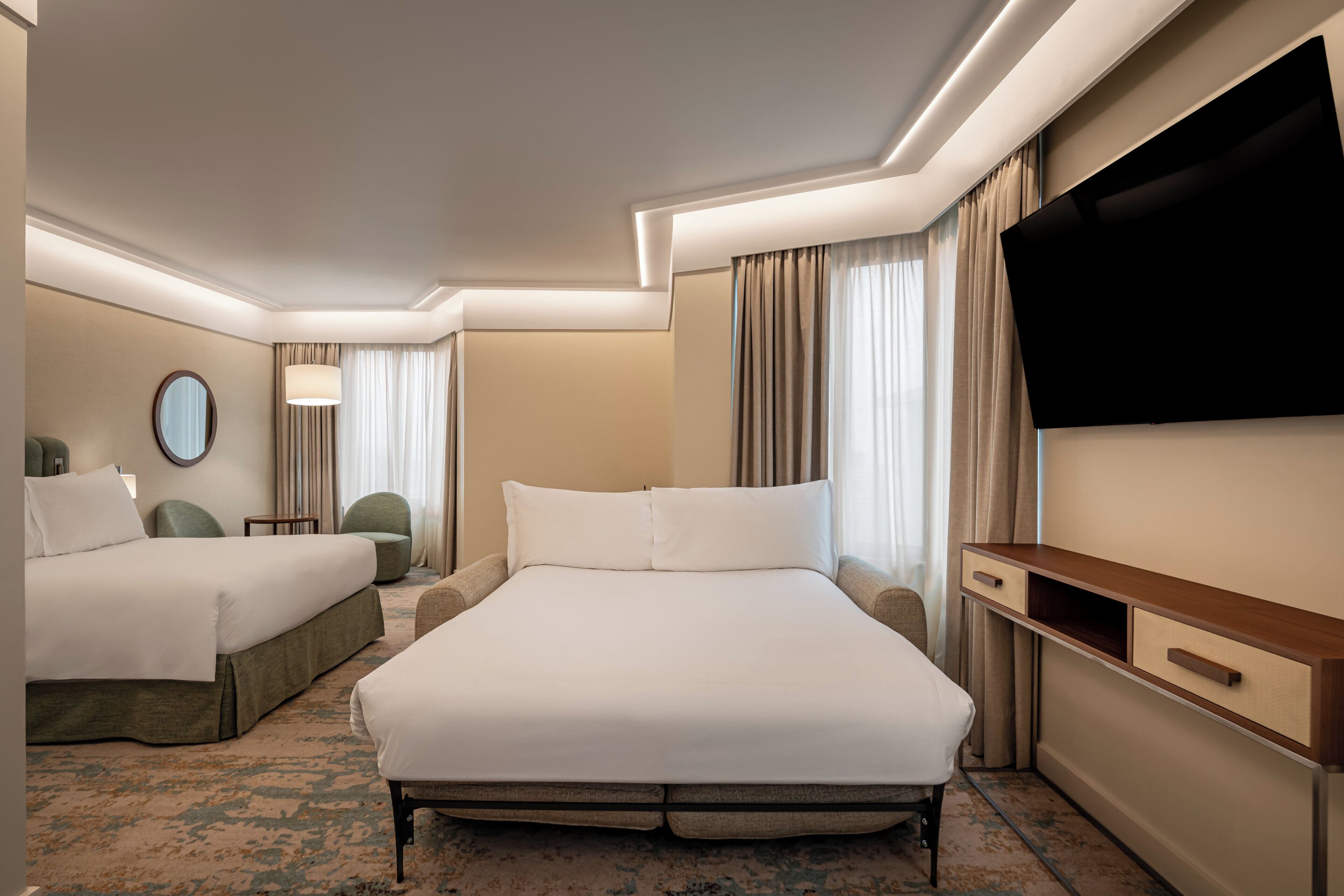 A hotel room with a large bed, a TV, a desk, and a chair.