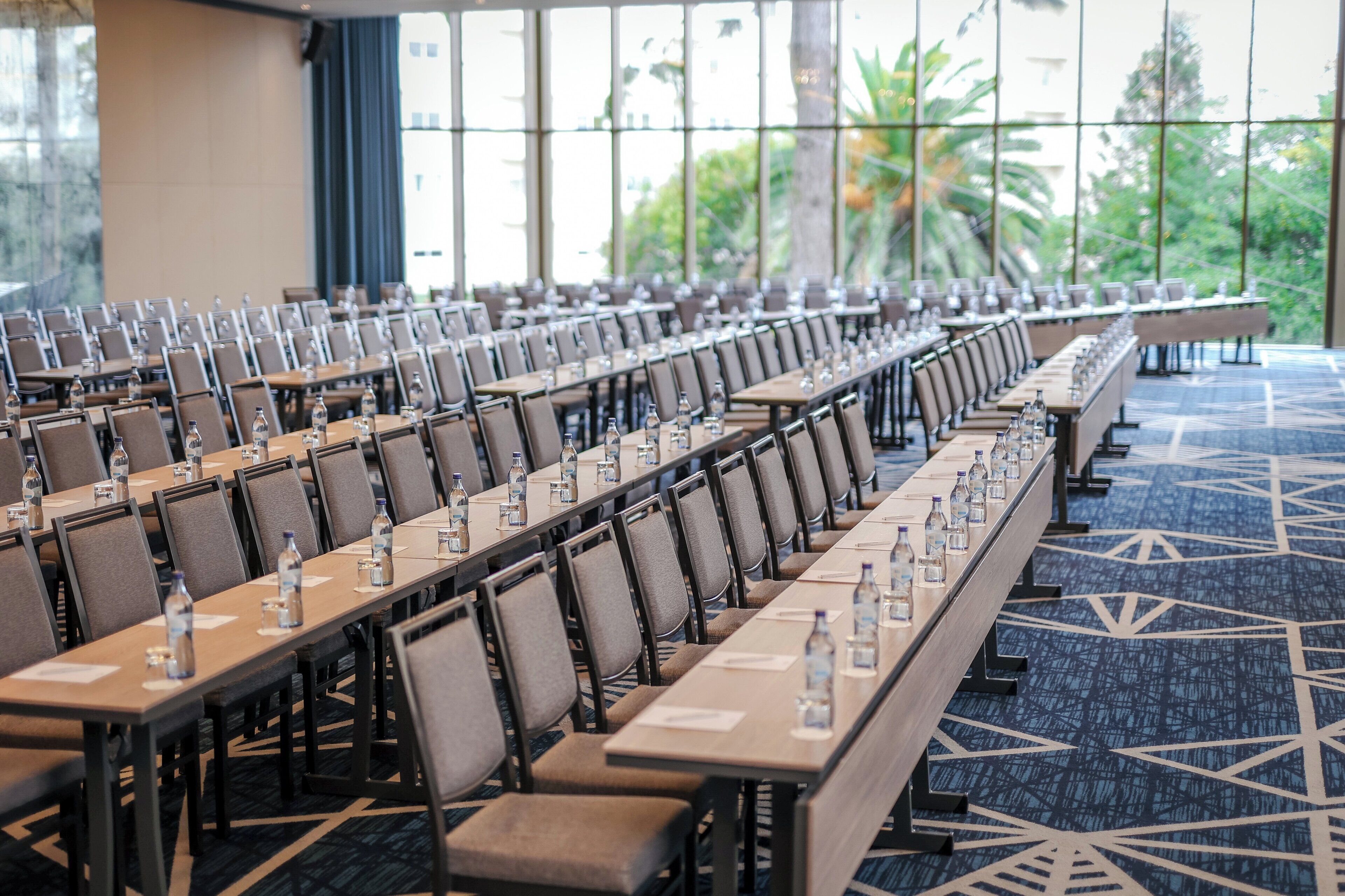 A conference room with long tables, chairs, water bottles, and papers.