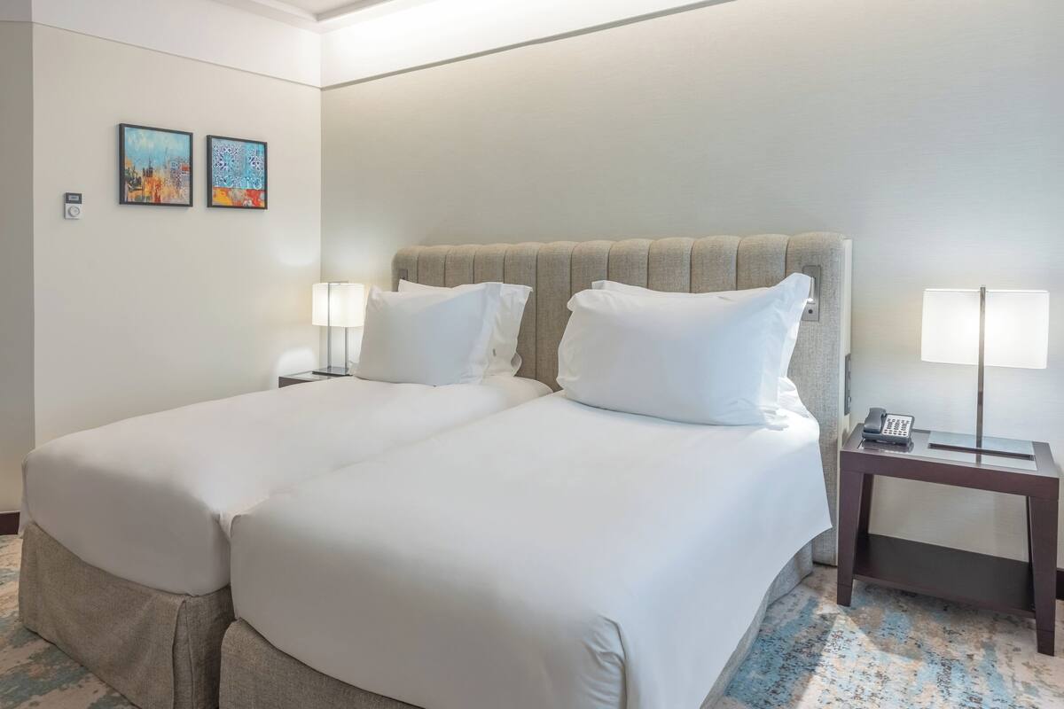 Habitación de hotel con dos camas, una mesita de noche, una lámpara y dos obras de arte en la pared.
