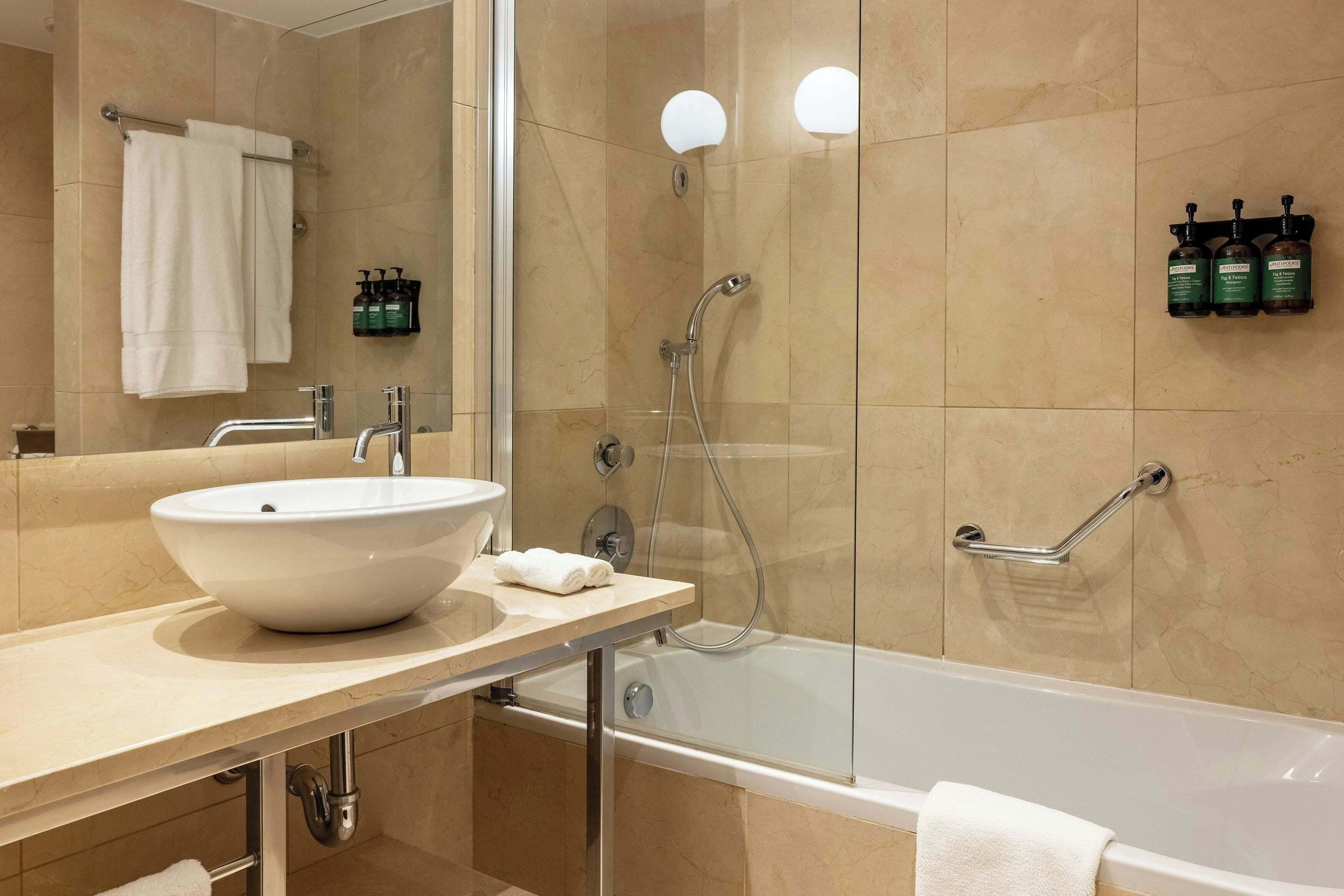 A modern bathroom with a large white sink, a glass-enclosed shower, and a bathtub.