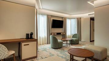 Habitación de hotel con escritorio, dos sillones, sofá, televisión y piso cubierto de alfombra.