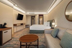 A hotel room with a bed, a sofa, a desk with a coffee maker, a TV mounted on the wall, and a mirror. - Crowne Plaza Porto by IHG (Porto)