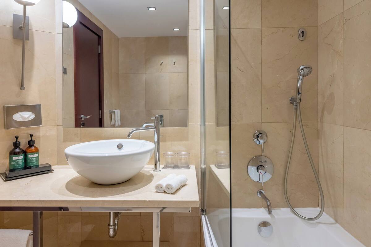 Un baño moderno con un lavamanos grande de color blanco, una cabina de ducha con paredes de vidrio y un espejo sobre el lavamanos.