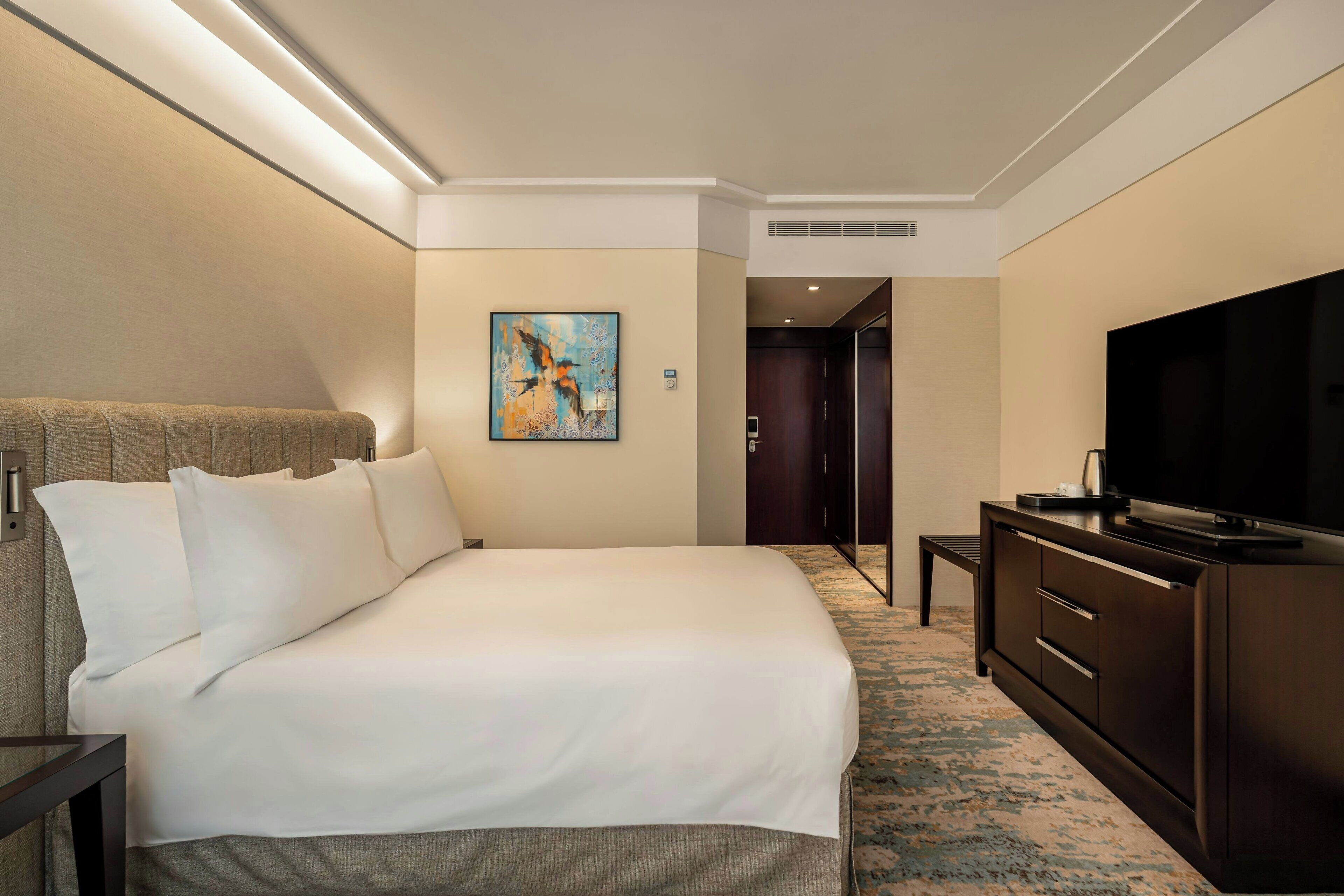 A hotel room with a large bed, a television, a small table, and a painting on the wall.