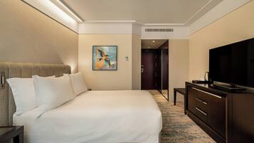 A hotel room with a large bed, a television, a small table, and a painting on the wall.