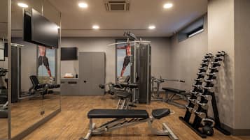 Un gimnasio con equipo de ejercicio, una banca, un espejo y un televisor.