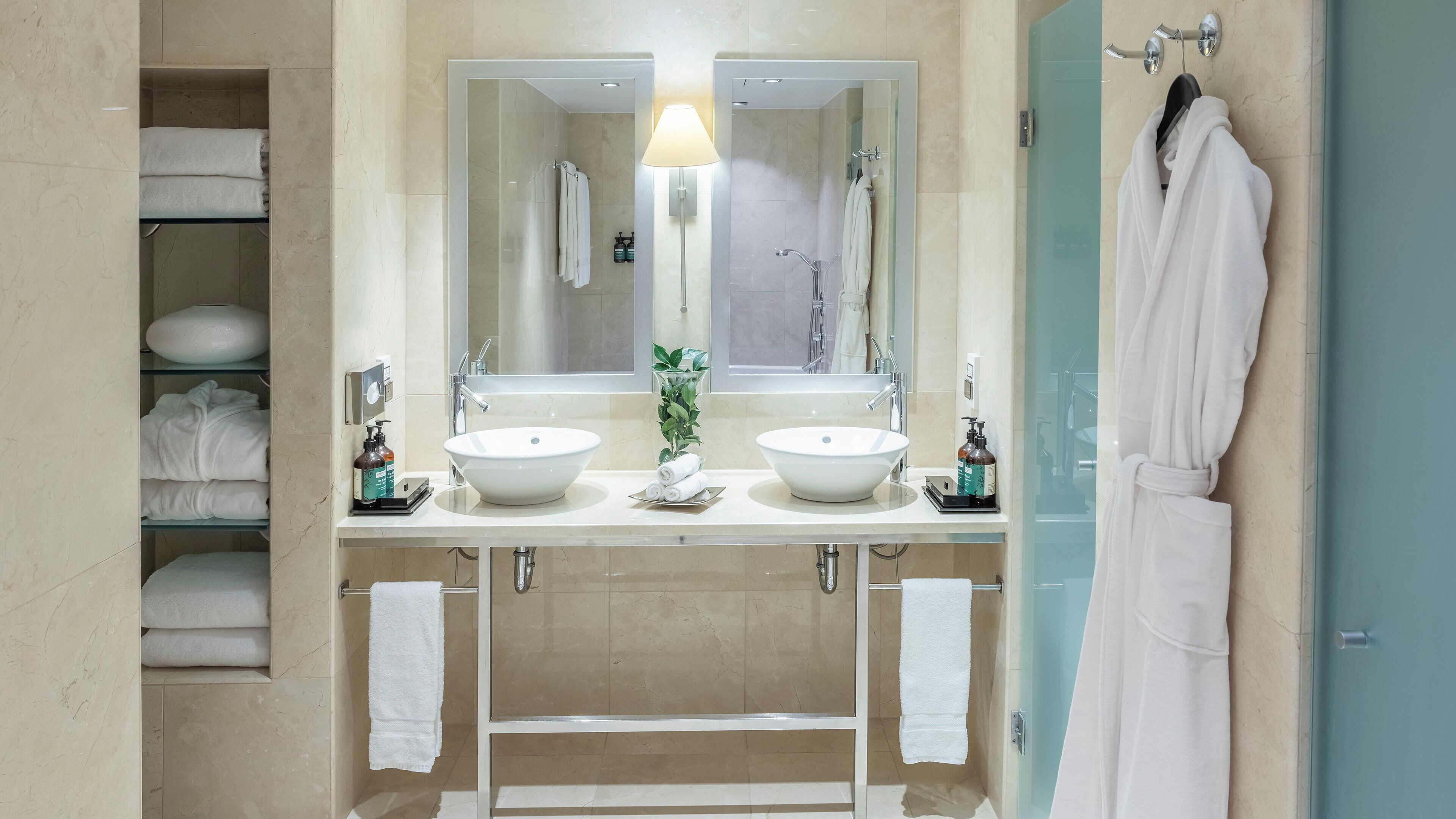 Une salle de bain avec deux lavabos, un grand miroir, un porte-serviettes et une cabine de douche en verre.