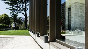 Un edificio moderno con fachada de vidrio, un camino pavimentado y un césped cuidado con árboles.