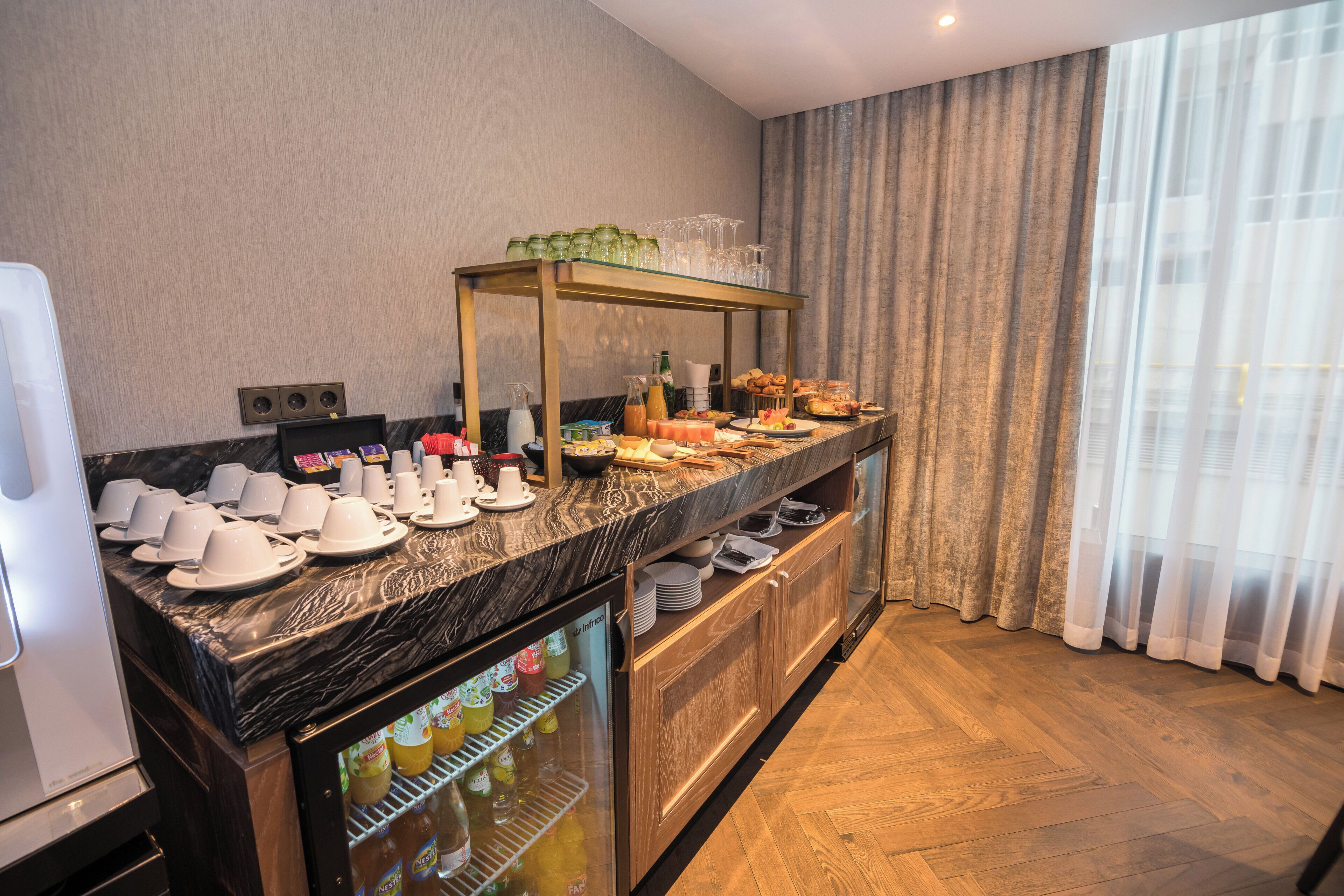 A hotel breakfast area with a marble countertop, a glass display case with beverages, and a buffet with various food items.