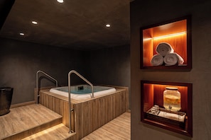 Un spa moderno con una bañera de madera, un juego de escalones y un estante con toallas y un tarro de sales de baño.