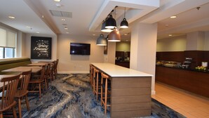 A modern hotel lobby with a marble-patterned floor, a bar area, and a seating area with wooden chairs and tables. - Fairfield Inn by Marriott Binghamton (Binghamton)