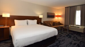 A hotel room with a large bed, a sofa, a small table, a lamp, a painting, and an air conditioning unit. - Fairfield Inn by Marriott Binghamton (Binghamton)