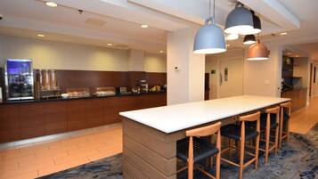 A modern kitchen with a central island, bar stools, pendant lighting, and a visible refrigerator.