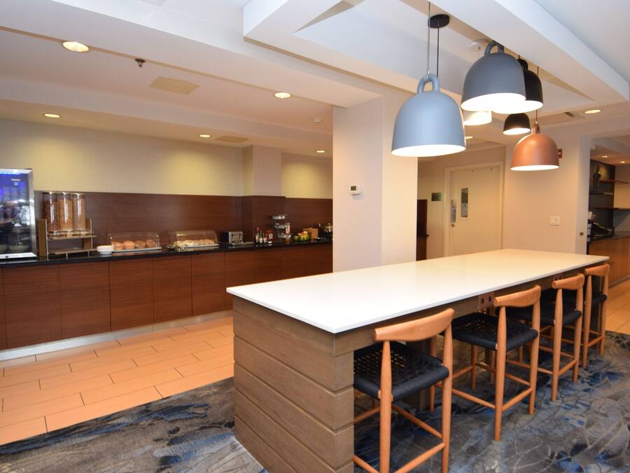 A modern kitchen with a central island, bar stools, pendant lighting, and a visible refrigerator.