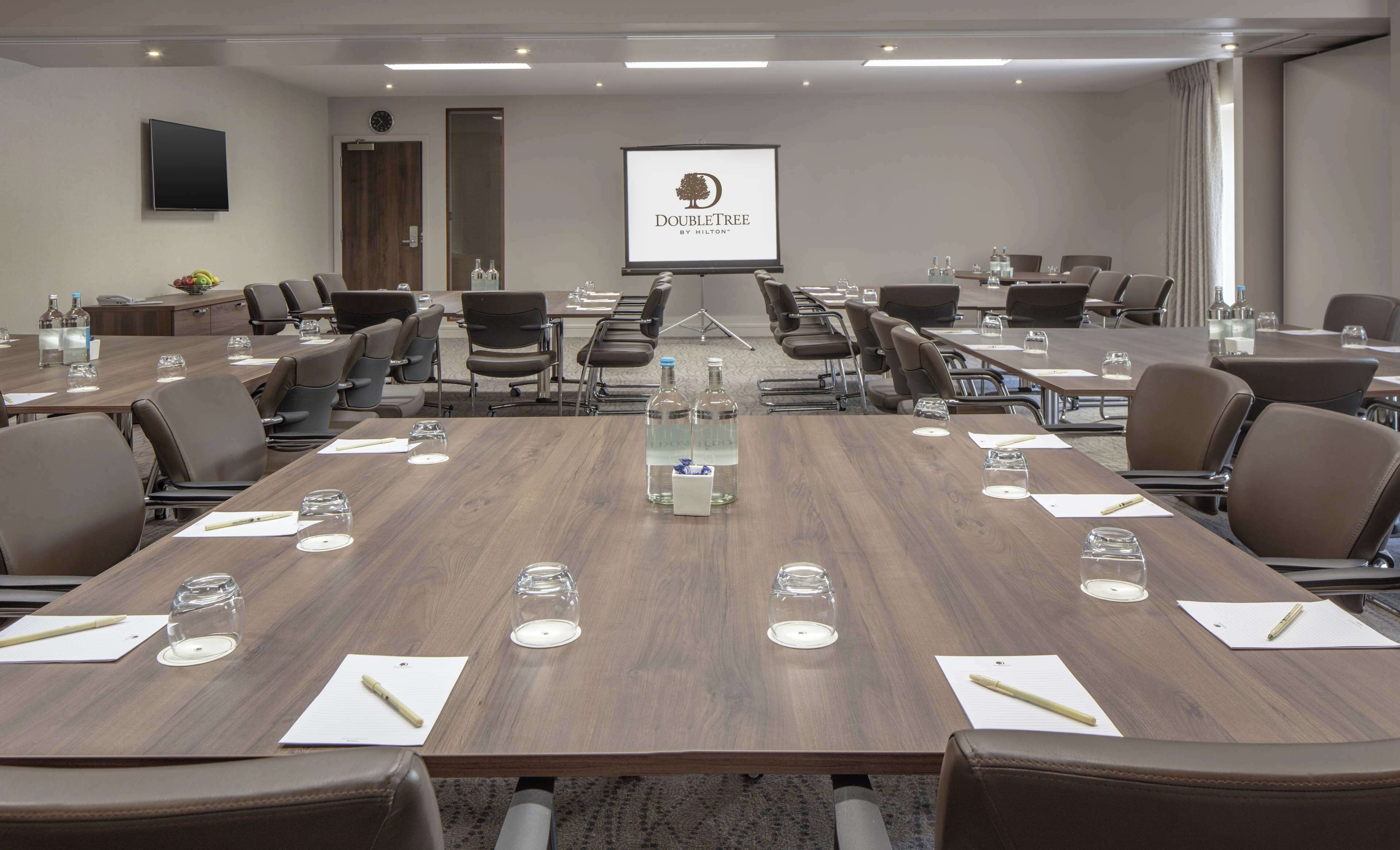 Una sala conferenze con diversi tavoli, sedie e un grande schermo che mostra il logo DoubleTree.