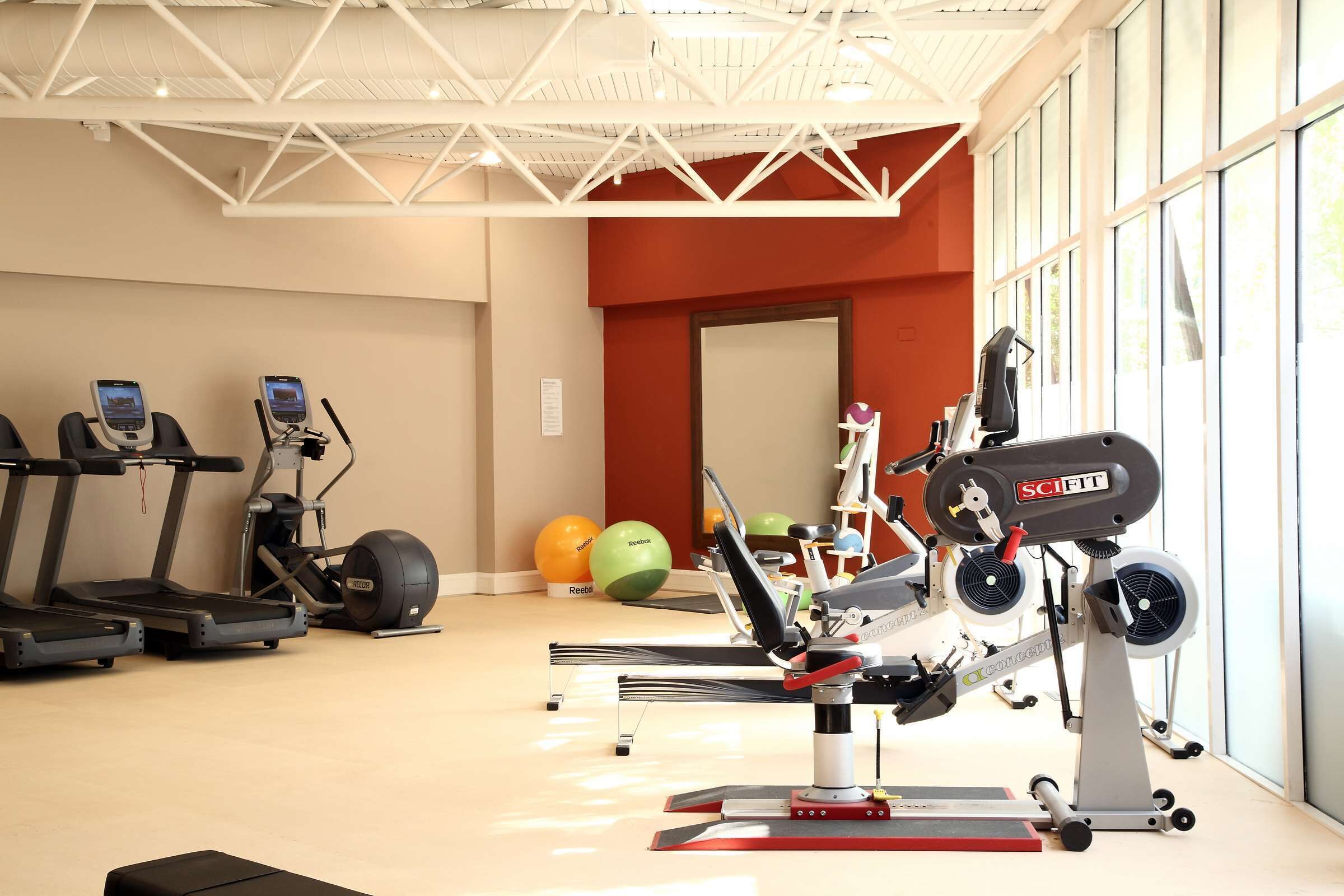 Een fitnessruimte met loopbanden, een roeimachine en fitnessballen.