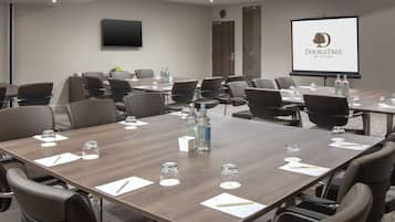 A conference room with a large table, multiple chairs, a projector screen, and a clock on the wall.